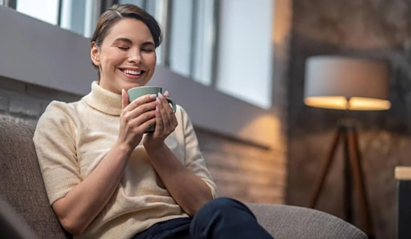 Smiling woman holding warm green mug in cozy room